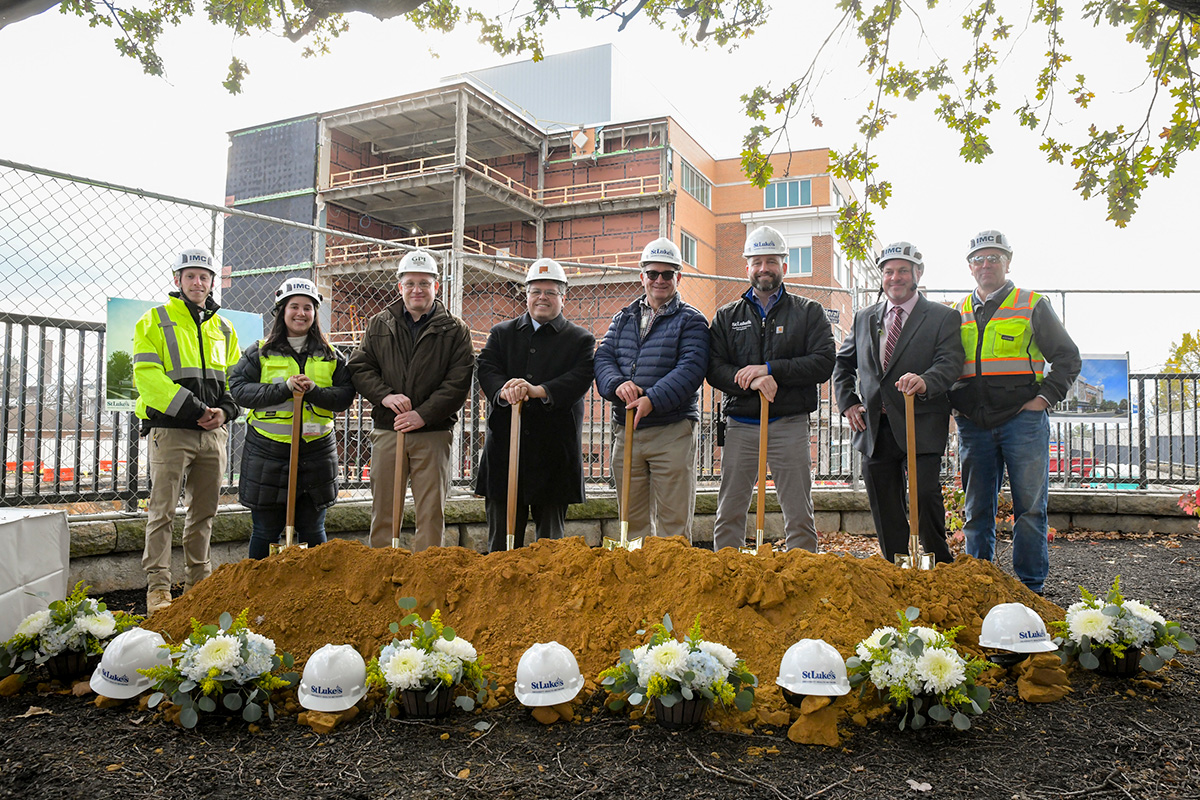 Several IMC employees in safety jackets and helmets posing for a photo in front of a dirt mound with safety helmets and with shovels in their hands