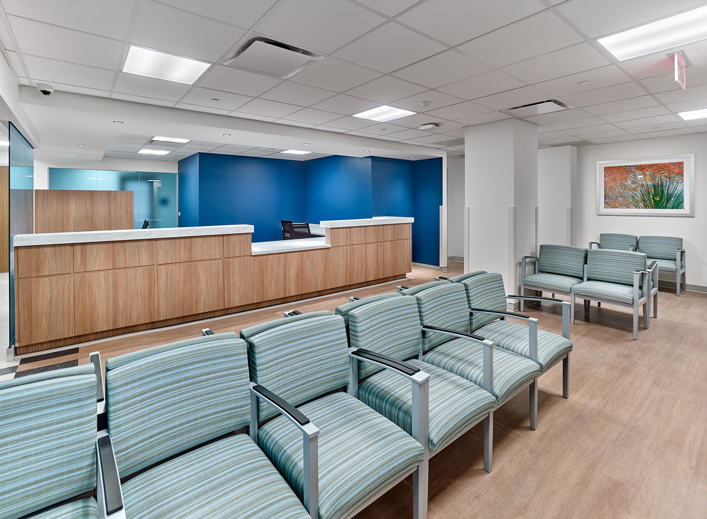 The reception room at ENT and Oral Surgery Suite at Jefferson Health featuring a row of light blue chairs with a wooden reception desks in the back
