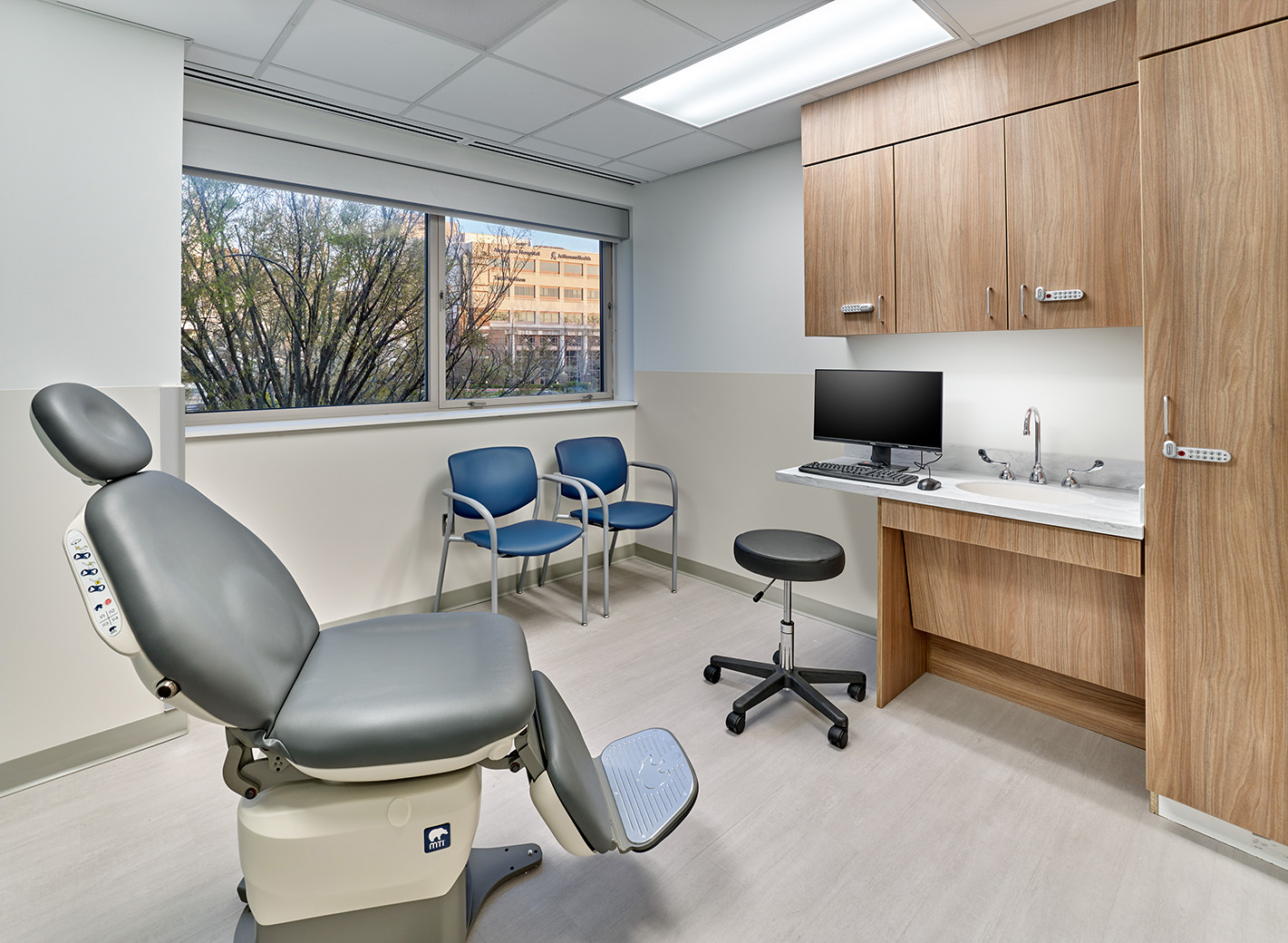 An exam room at ENT and Oral Surgery Suite at Jefferson Health featuring a gray oral surgery chair in the center of the room and a computer screen and wood cabinets
