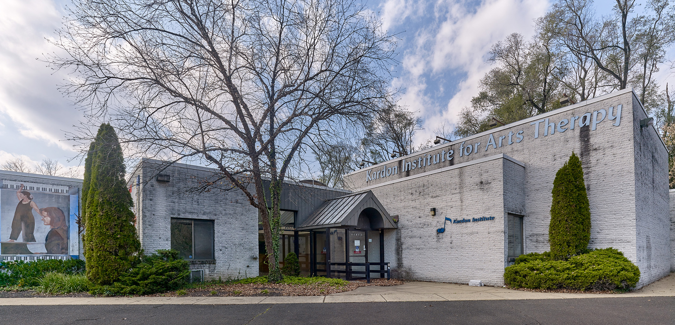 The exterior of a gray brick building with a glass entrance and a tree in front