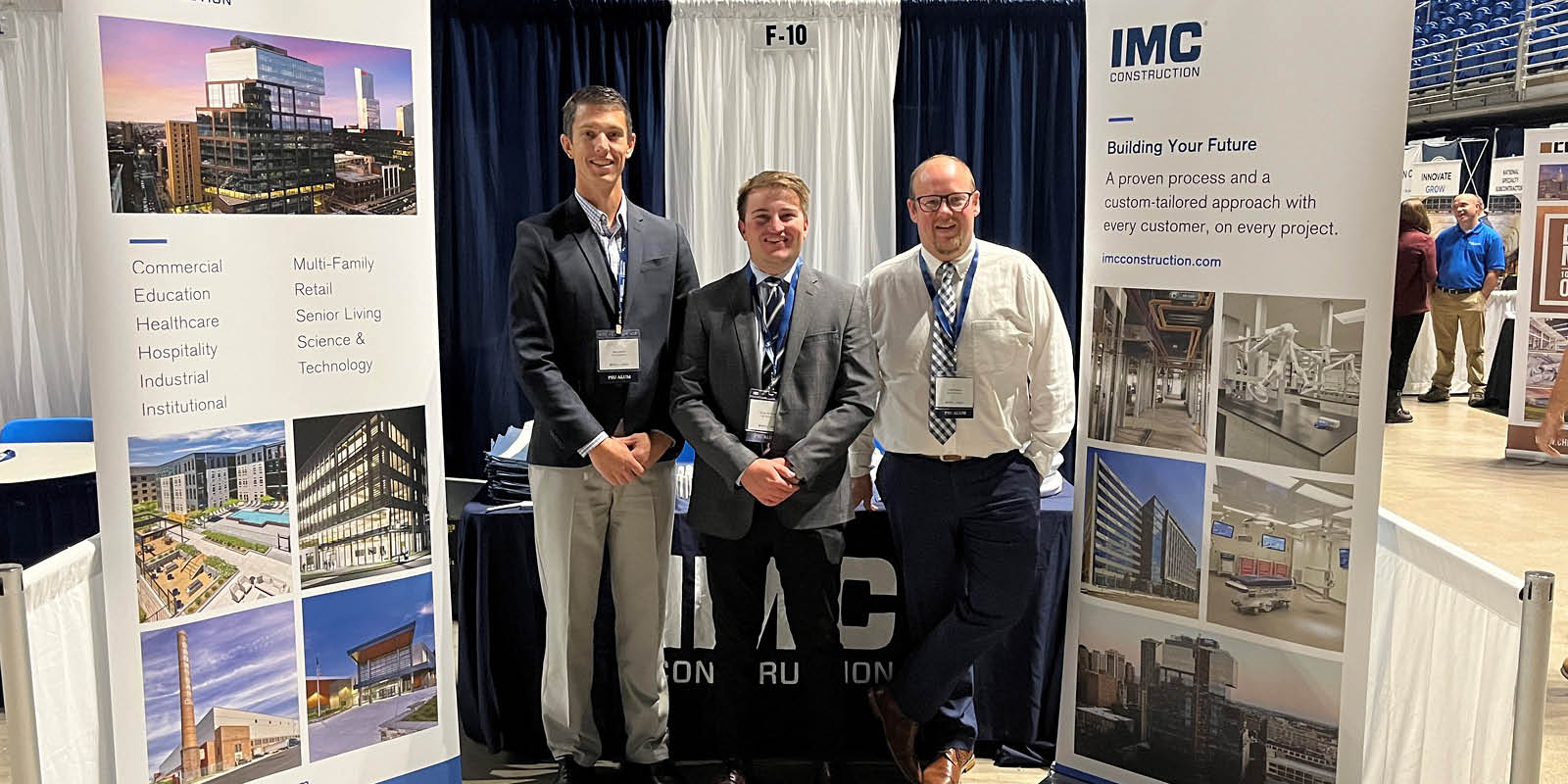Three IMC employees at Penn State University's 2023 Career Fair standing in front of table with IMC banners