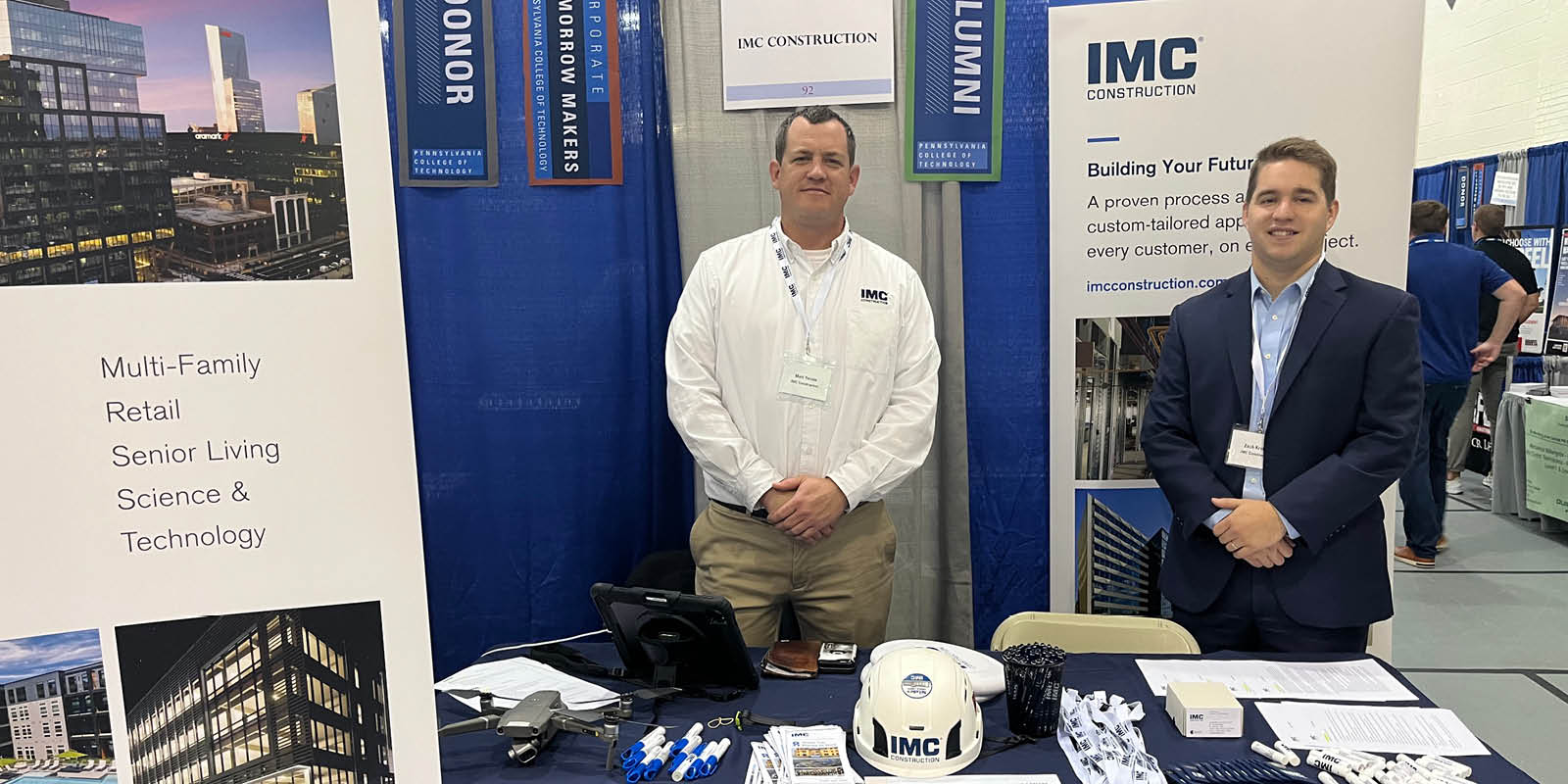 Two IMC employees at a 2023 Career Fair standing in front of table with IMC banners